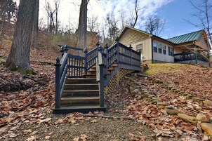 A wooden staircase leading to a house with a green roof, surrounded by trees and fallen leaves.