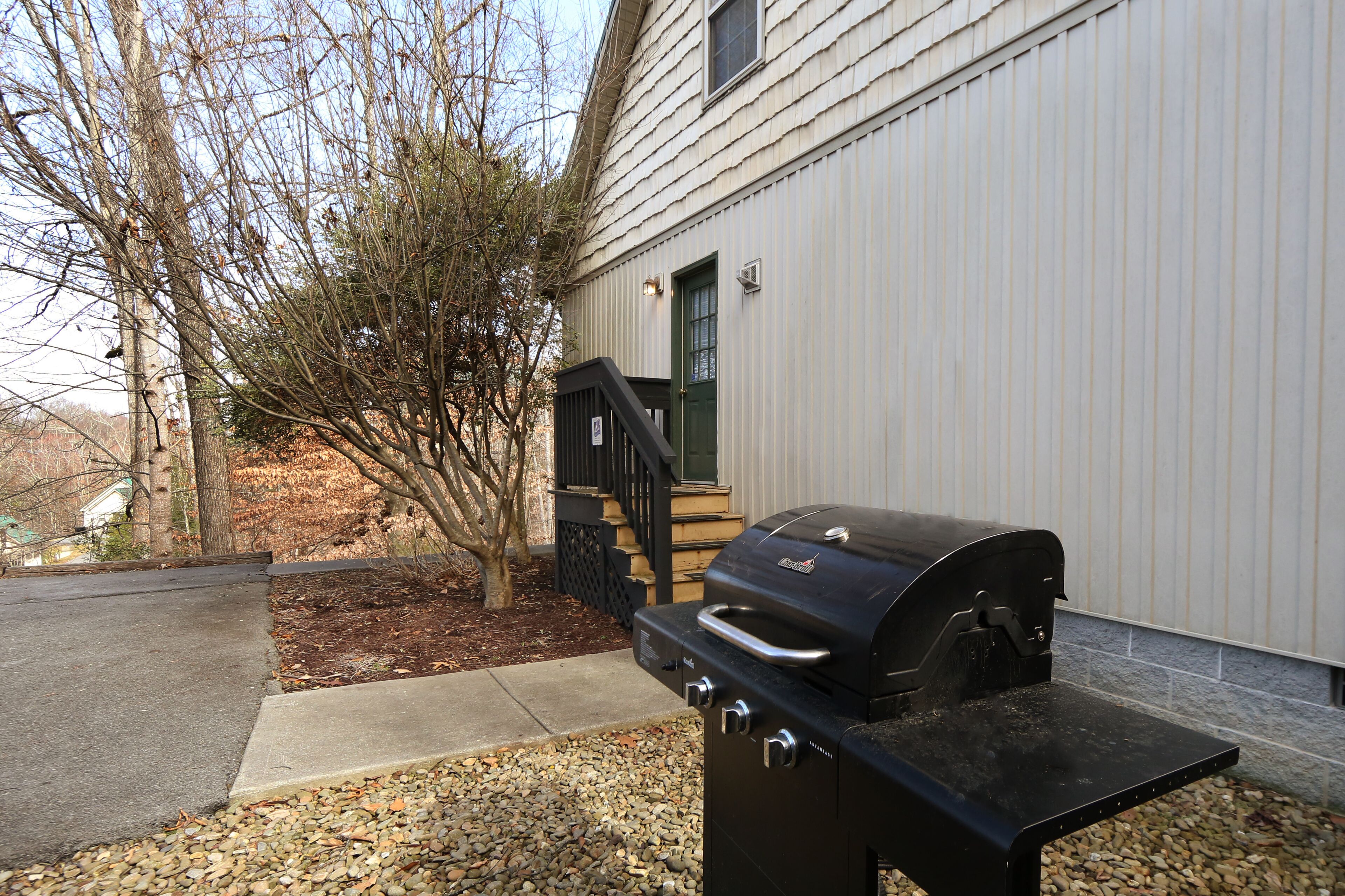Una parrilla de barbacoa frente a una casa con terraza de madera y puerta verde.