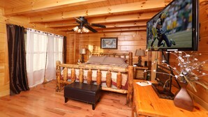 A wooden cabin bedroom with a bed, a ceiling fan, a TV, and a wooden dresser.