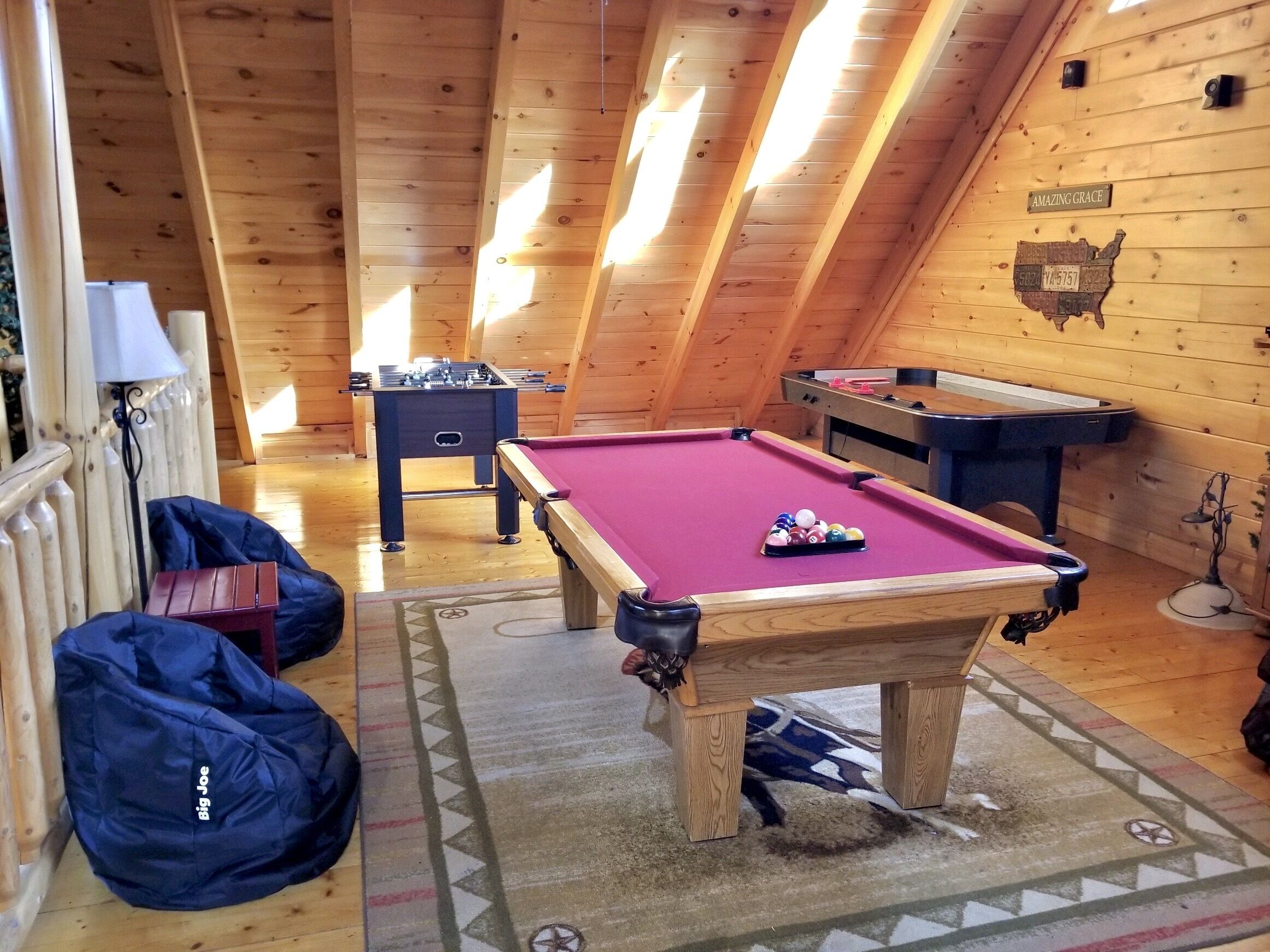 A cozy, wooden-floored game room with a pool table, foosball table, and a poker table.