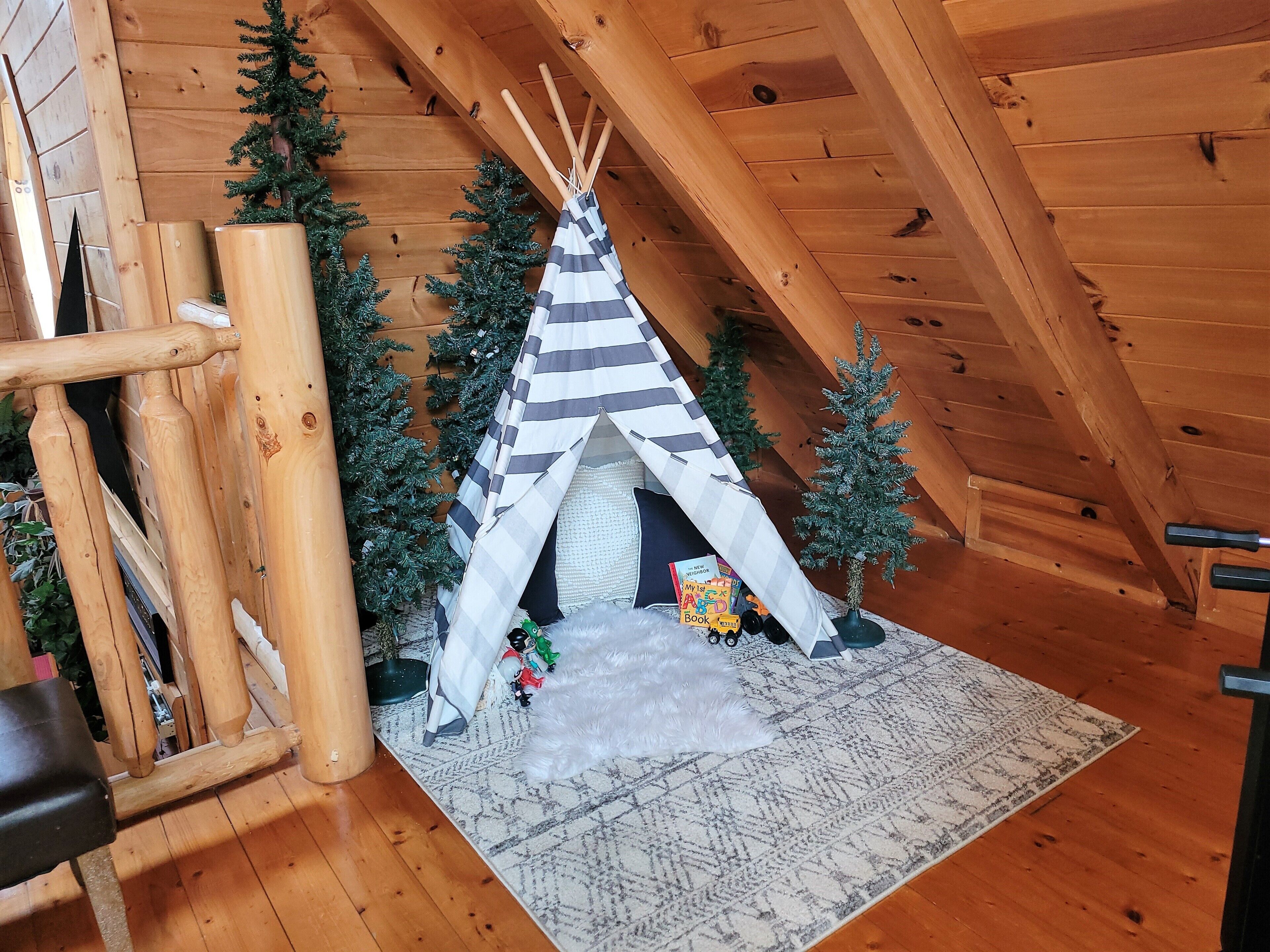 Acogedor cuarto en ático con techo inclinado de madera, un pequeño tipi y árboles de Navidad.