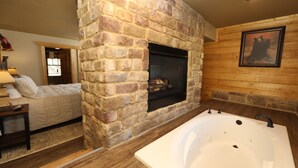 A room with a stone fireplace, a large bathtub, and a bed with a nightstand. - Splash Time Cinema - Six Bedroom Chalet (Gatlinburg)