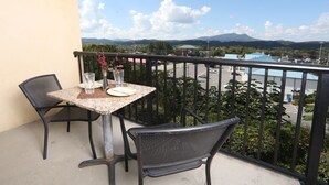 A balcony with a table and chairs, a vase with flowers, and a view of a parking area and buildings in the distance. - Mountain View Condo 1205 - Two Bedroom Condo (Pigeon Forge)