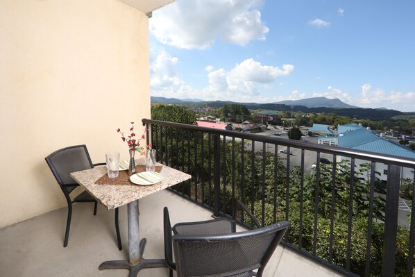 A balcony with a table set for two, chairs, and a vase with flowers. - Mountain View Condo 1205 - Two Bedroom Condo (Pigeon Forge)