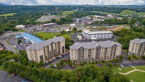 A multi-story hotel with a swimming pool, surrounded by parking and greenery. - Mountain View Condo 1205 - Two Bedroom Condo (Pigeon Forge)