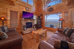 A cozy cabin interior with a stone fireplace, leather couches, a flat-screen TV, and a balcony with a view. - I Can Only Imagine - One Bedroom Cabin (Sevierville)