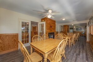A dining area with a wooden table and chairs, a ceiling fan, and a fireplace. - Magnolia Place 5 - Eight Bedroom Chalet (Pigeon Forge)