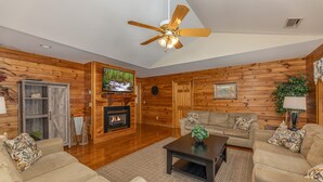 Ein gemütliches Wohnzimmer mit Kamin, Holzwänden, Fernseher und Deckenventilator.