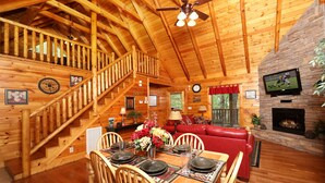 L’intérieur d’un chalet en bois comprend un coin repas, un canapé en cuir rouge, une cheminée et un escalier.