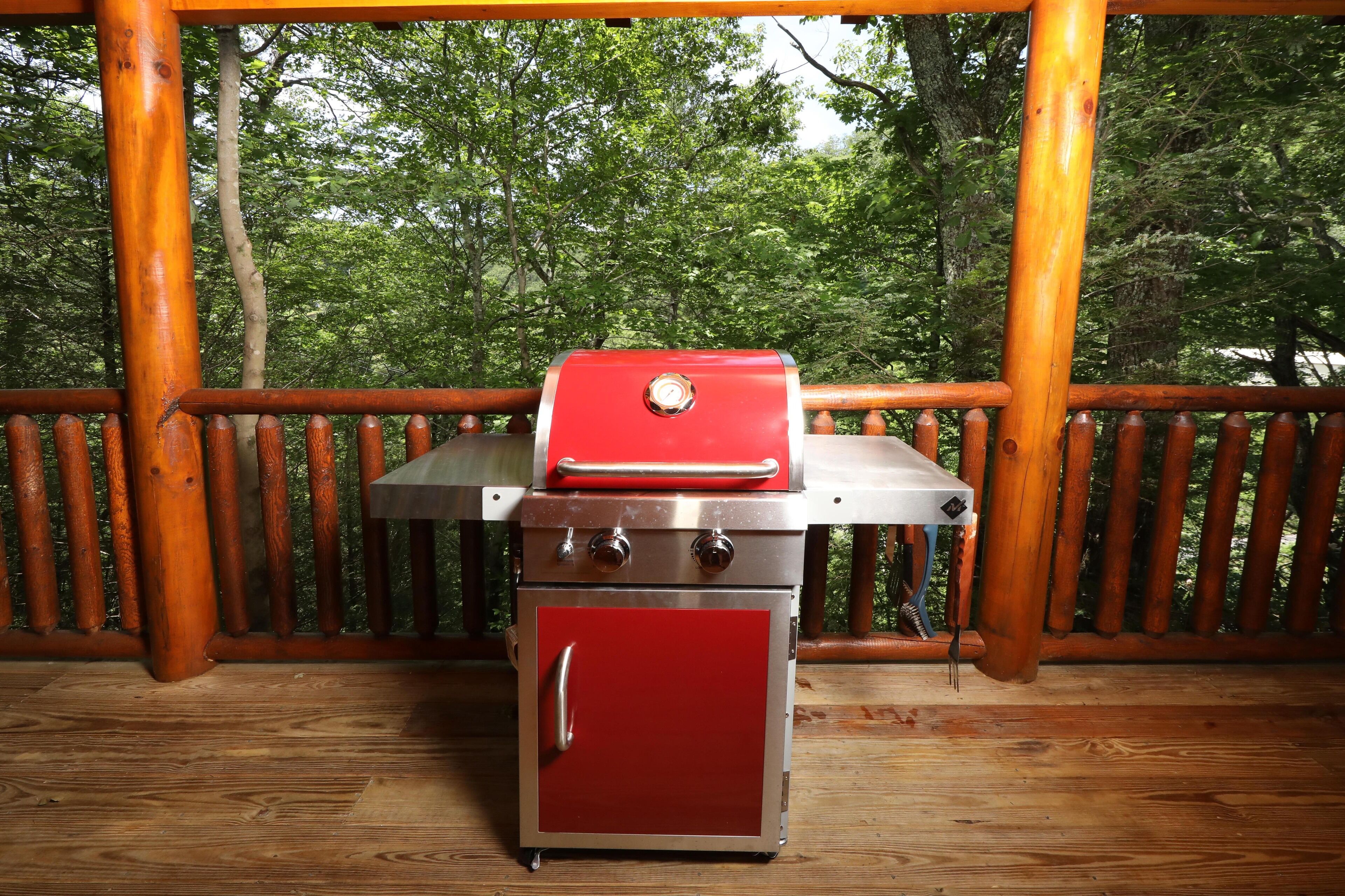 Un barbecue portable doté d’un meuble rouge et d’un dessus en acier inoxydable, placé sur une terrasse en bois avec une rambarde en bois.