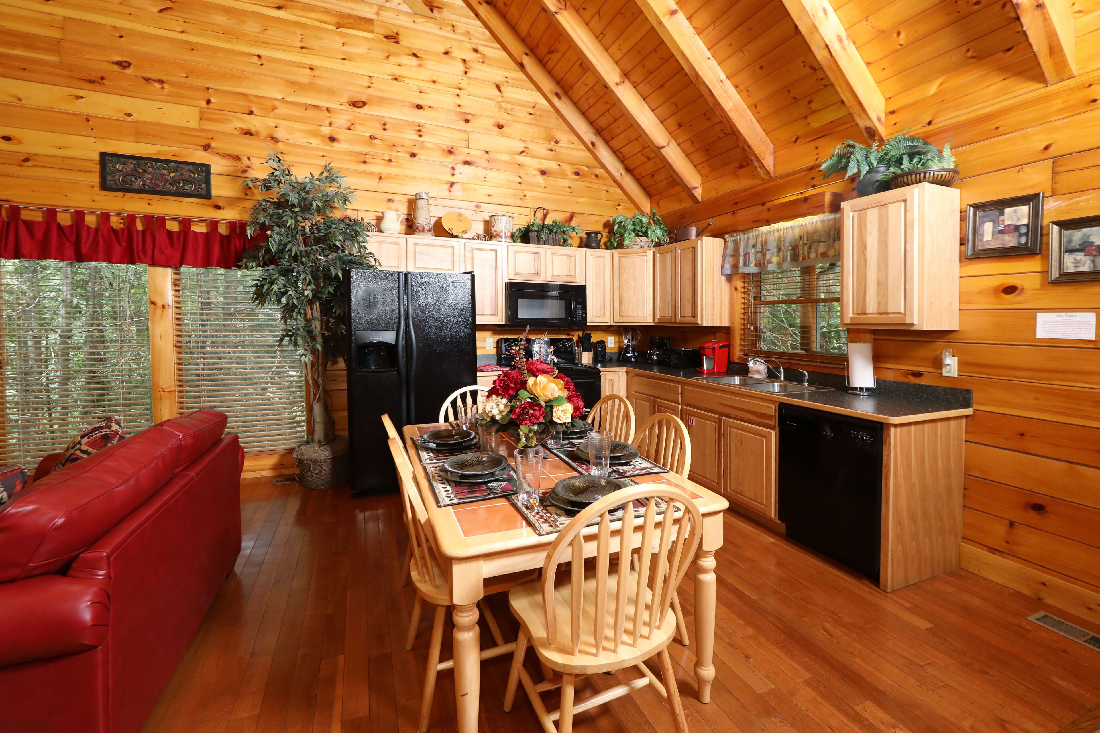 A wooden cabin interior with a dining area, kitchen, and red sofa.