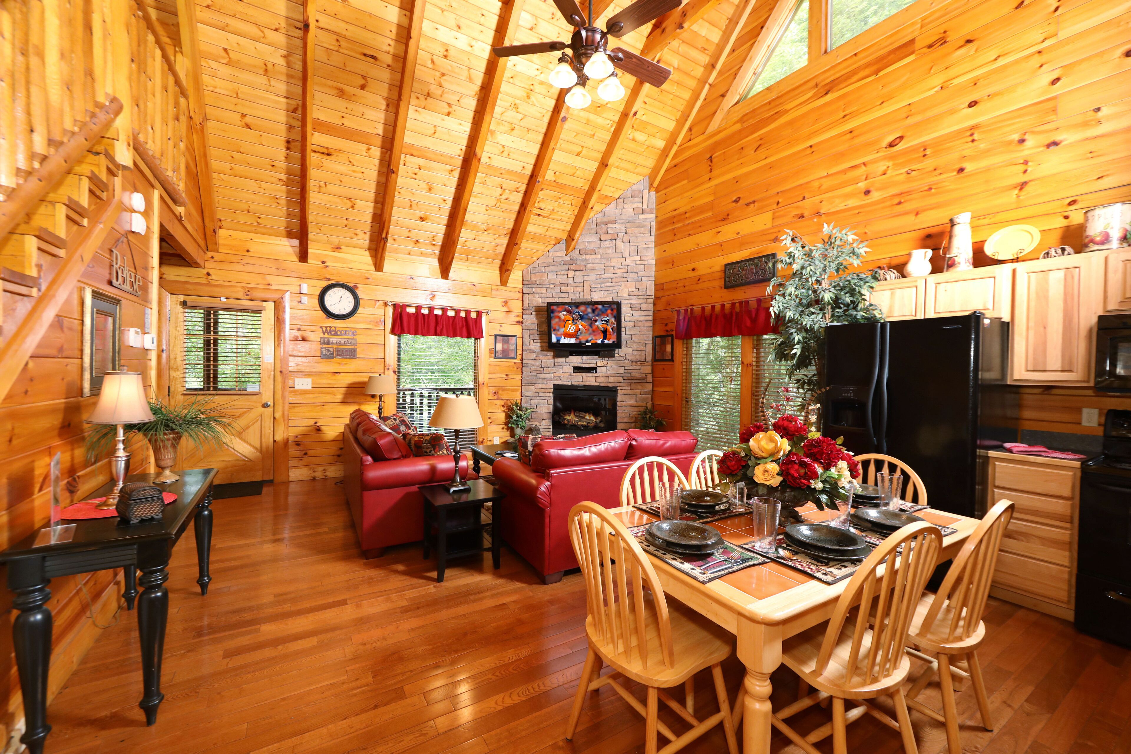 A cozy log cabin interior with a dining area, red leather sofa, wooden dining table, and a fireplace.