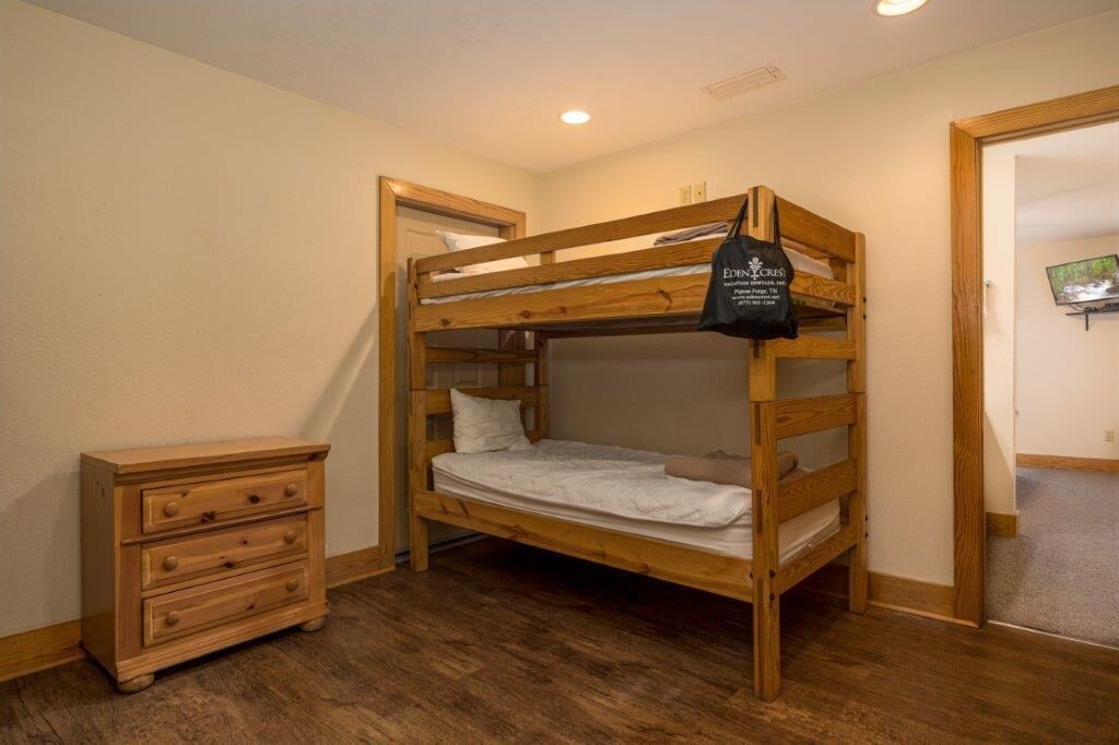 A bunk bed with a wooden frame, a small wooden dresser, and a television on the wall.