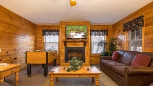 A cozy room with wooden walls, a fireplace, a sofa, a coffee table, and a foosball table. - Briarstone Lodge Condo 13F - Three Bedroom Condo (Pigeon Forge)