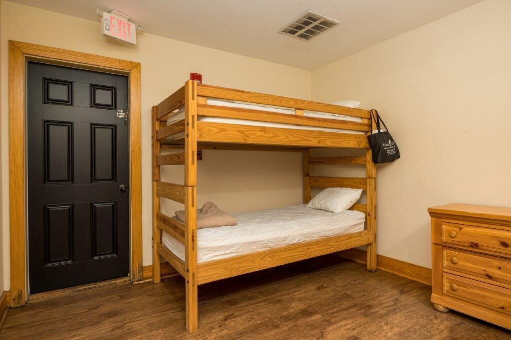 A bunk bed with a wooden frame, a black door with an exit sign, and a wooden dresser.