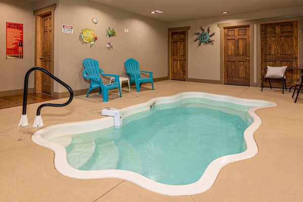 An indoor swimming pool with a wavy edge, surrounded by blue chairs, wooden doors, and a wall with decorative fish and a sun design. - Hilltop Haven - Four Bedroom Chalet (Gatlinburg)