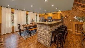 A kitchen with wooden cabinets, a stone island, and a dining area with a table and chairs. - Hilltop Haven - Four Bedroom Chalet (Gatlinburg)