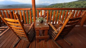 Terraza de madera con una mesa y sillas, con vistas a un paisaje montañoso.