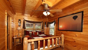 Un dormitorio de cabaña rústica con una cama de madera, un ventilador de techo y un gran ventanal con vistas al exterior.