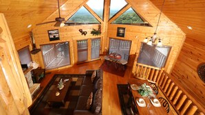Interior de una cabaña de troncos con comedor, sofá y chimenea.