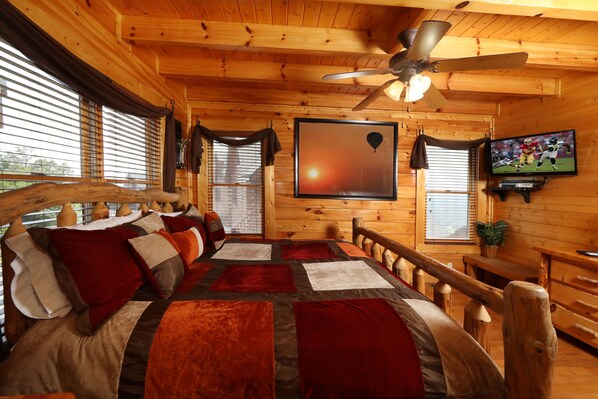 A wooden cabin room with a bed, a ceiling fan, a television, and a window with blinds. - Up Up Away - Two Bedroom Cabin (Sevierville)
