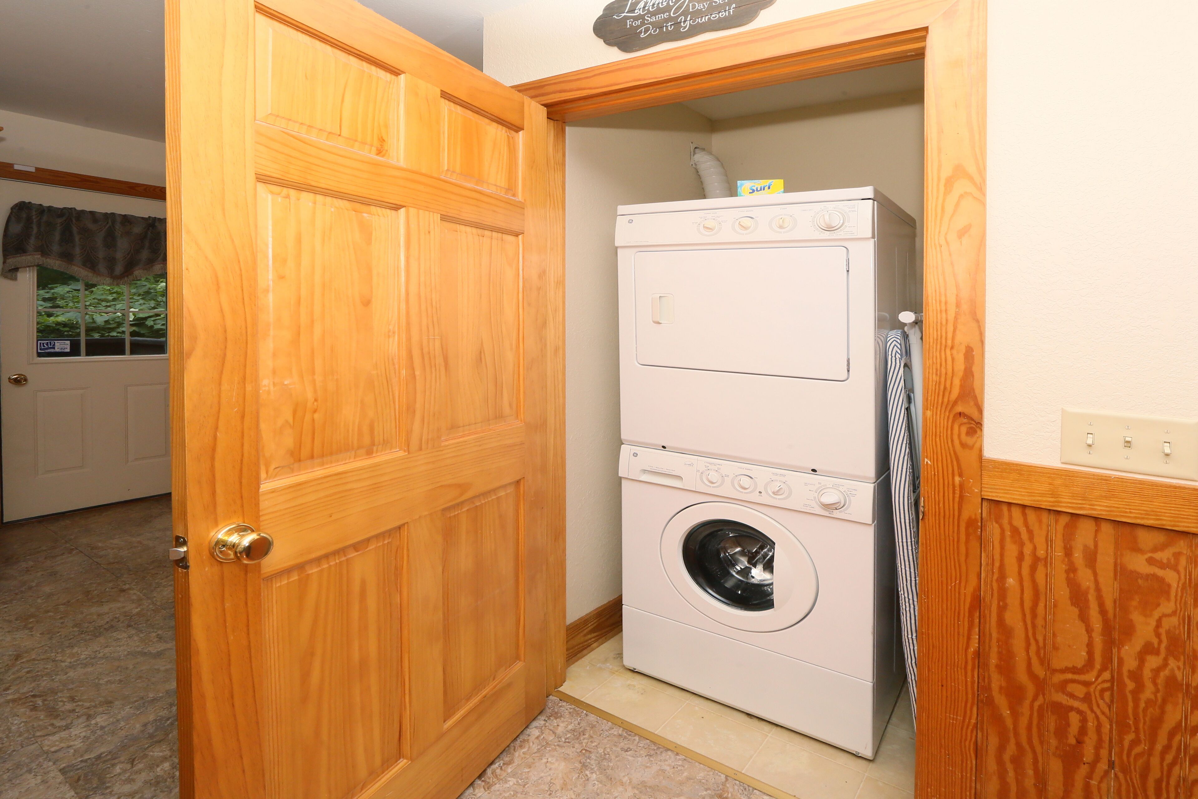 A laundry room with a stacked washer and dryer, wooden door, and a sign on the wall.