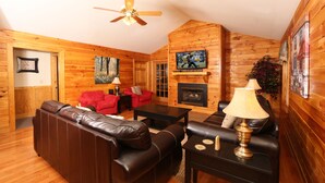 A cozy log cabin interior with a fireplace, leather sofas, a television, and a ceiling fan. - Holly Grove 1 - Three Bedroom Chalet (Pigeon Forge)