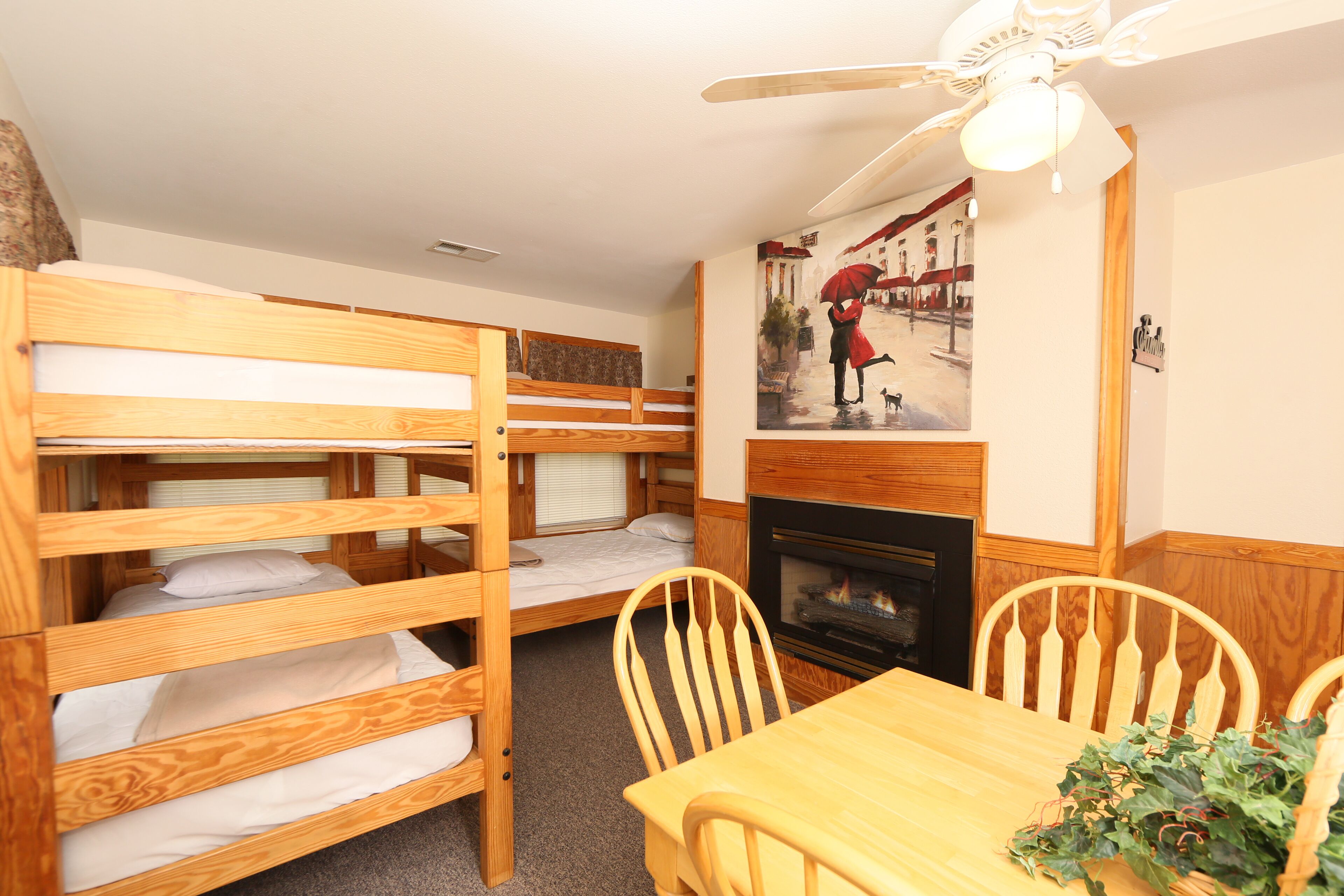 A bunk bed room with a dining table and chairs, a fireplace, and a ceiling fan.