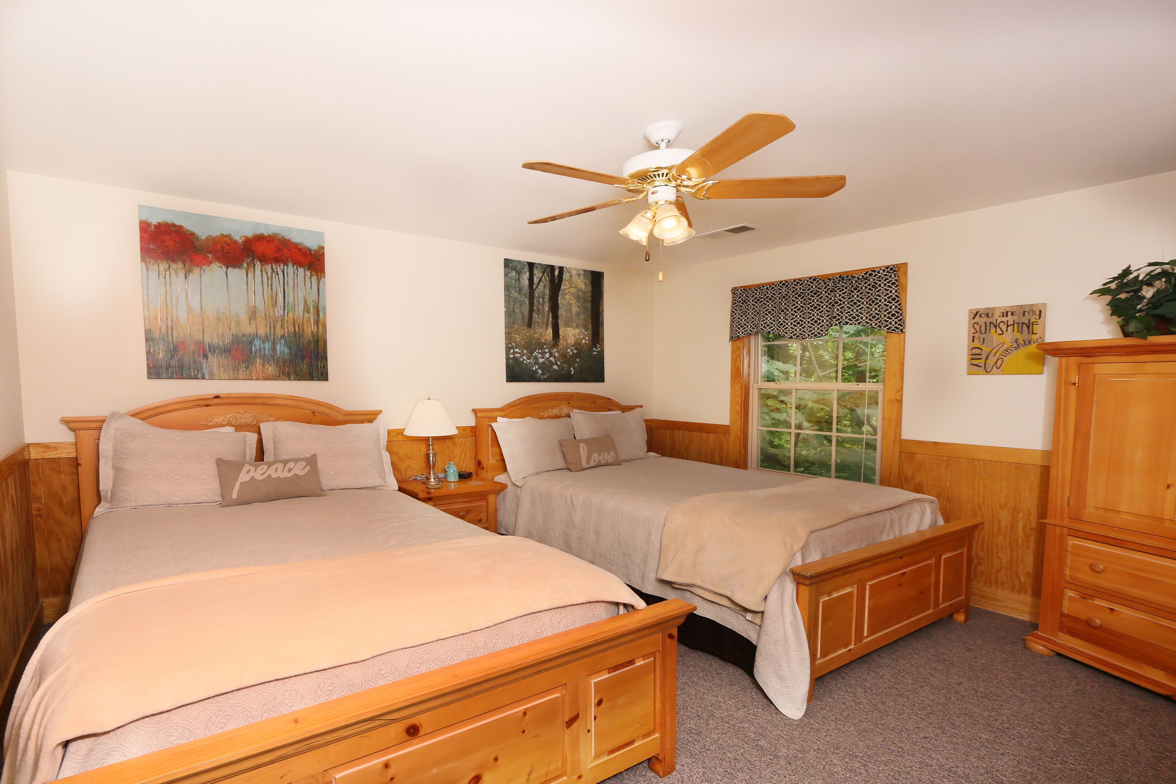 A bedroom with two beds, a ceiling fan, and artwork on the walls.
