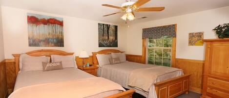 A bedroom with two beds, a ceiling fan, and artwork on the walls.