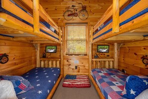 A cabin with two beds, wooden walls, a bicycle, and a television on the wall. - Picture Perfect- Seven Bedroom Cabin (Sevierville)