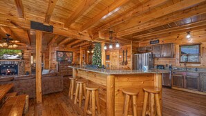 A log cabin interior with a wooden bar, stools, a fireplace, a Christmas tree, and a kitchen area. - Picture Perfect- Seven Bedroom Cabin (Sevierville)