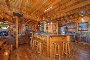 A wooden cabin interior with a bar area, wooden stools, a fireplace, and a Christmas tree.