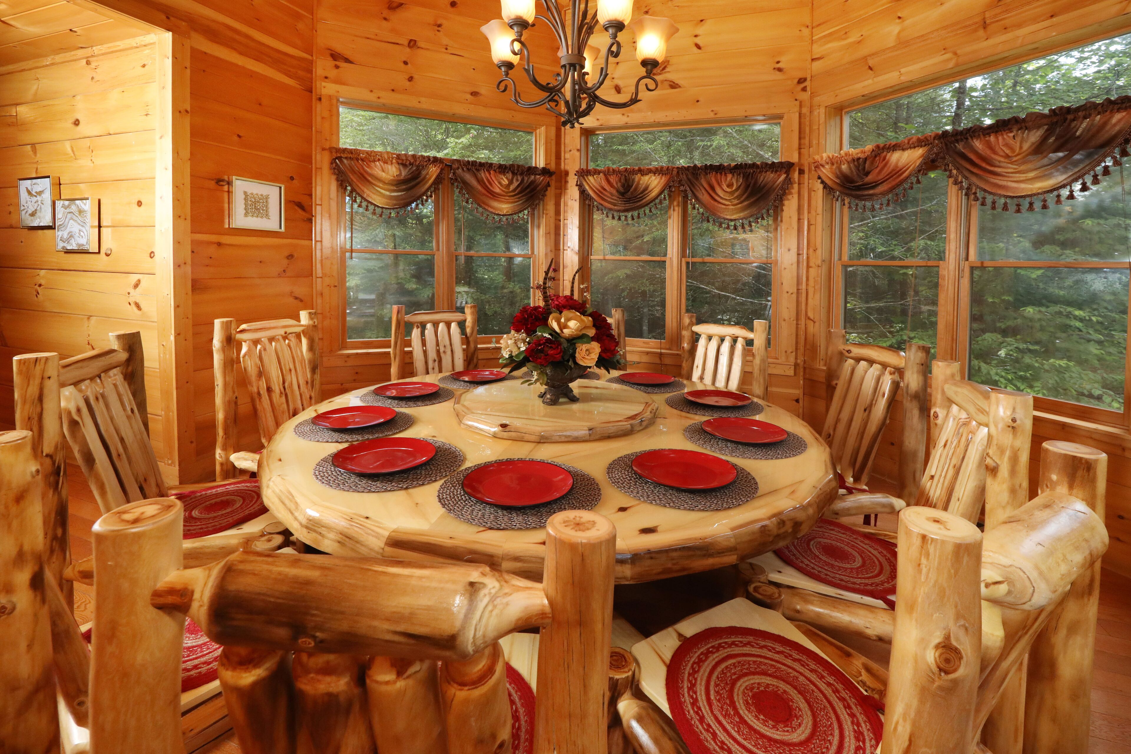 A wooden dining room with a round table, red and white plates, and a chandelier.