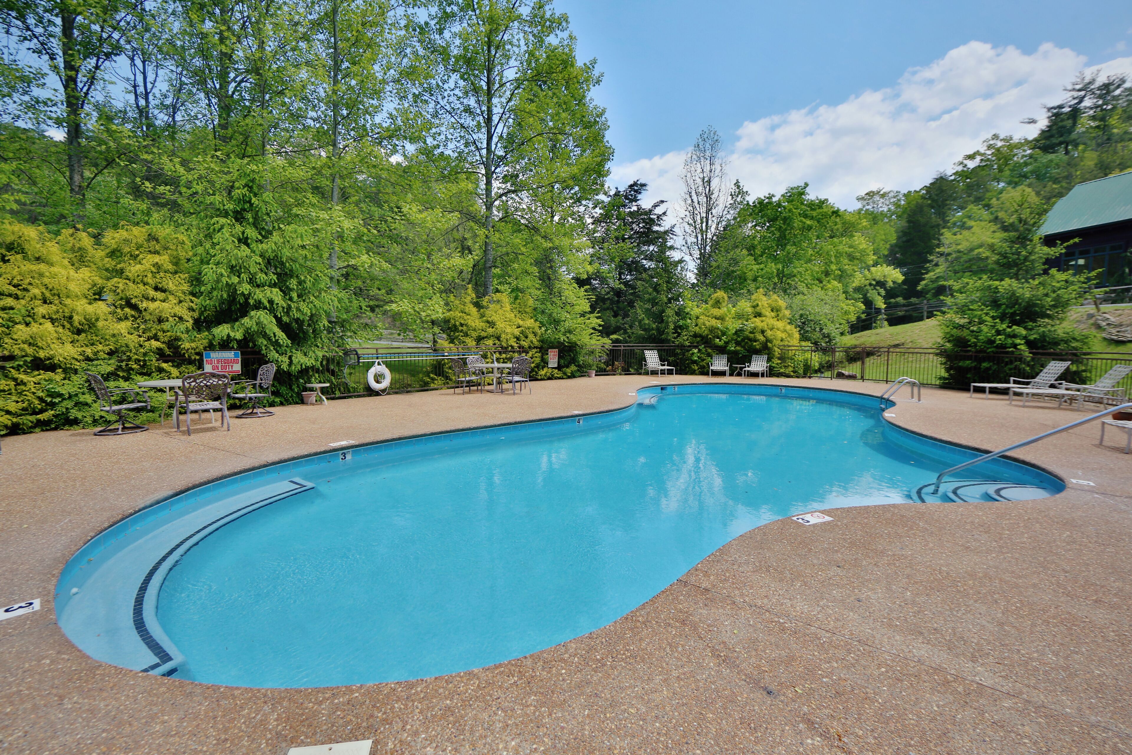 A swimming pool with a curved edge, surrounded by lounge chairs and a paved deck.