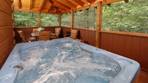 Una cabaña de madera con jacuzzi, terraza de madera y amplios ventanales con vista a un bosque.