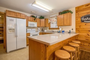 A kitchen with wooden cabinets, a white refrigerator, a microwave, a coffee maker, and a sign that says "Baked Goods".