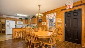 Interior de madera con una mesa de comedor, sillas, un refrigerador, un microondas y una puerta negra con un letrero de SALIDA.