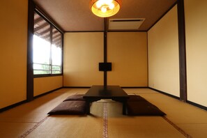 A traditional tatami room with a low table and cushions, large windows, and a ceiling light fixture. - Tabinoyado Asonoyu (Aso)