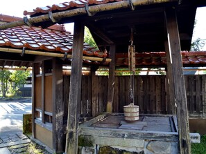 A traditional Japanese structure with a tiled roof, wooden pillars, and a stone platform with a water feature. - Tabinoyado Asonoyu (Aso)