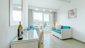 A modern hotel room with a dining area, a sofa, and a balcony with a view of the mountains.