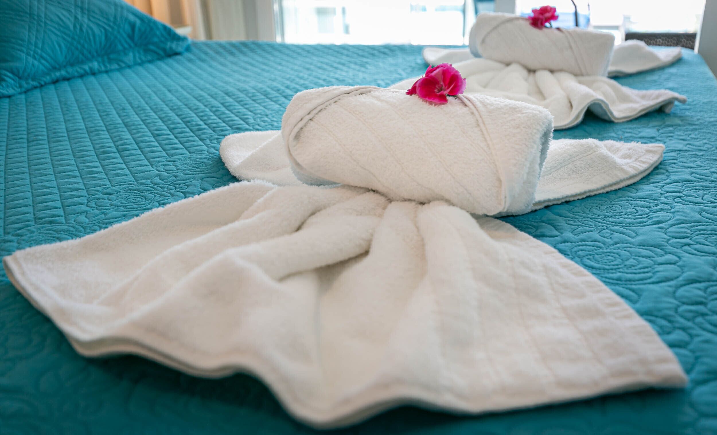 A bed with a teal quilted bedspread and two white towels with pink flowers, indicating a hotel room setting.