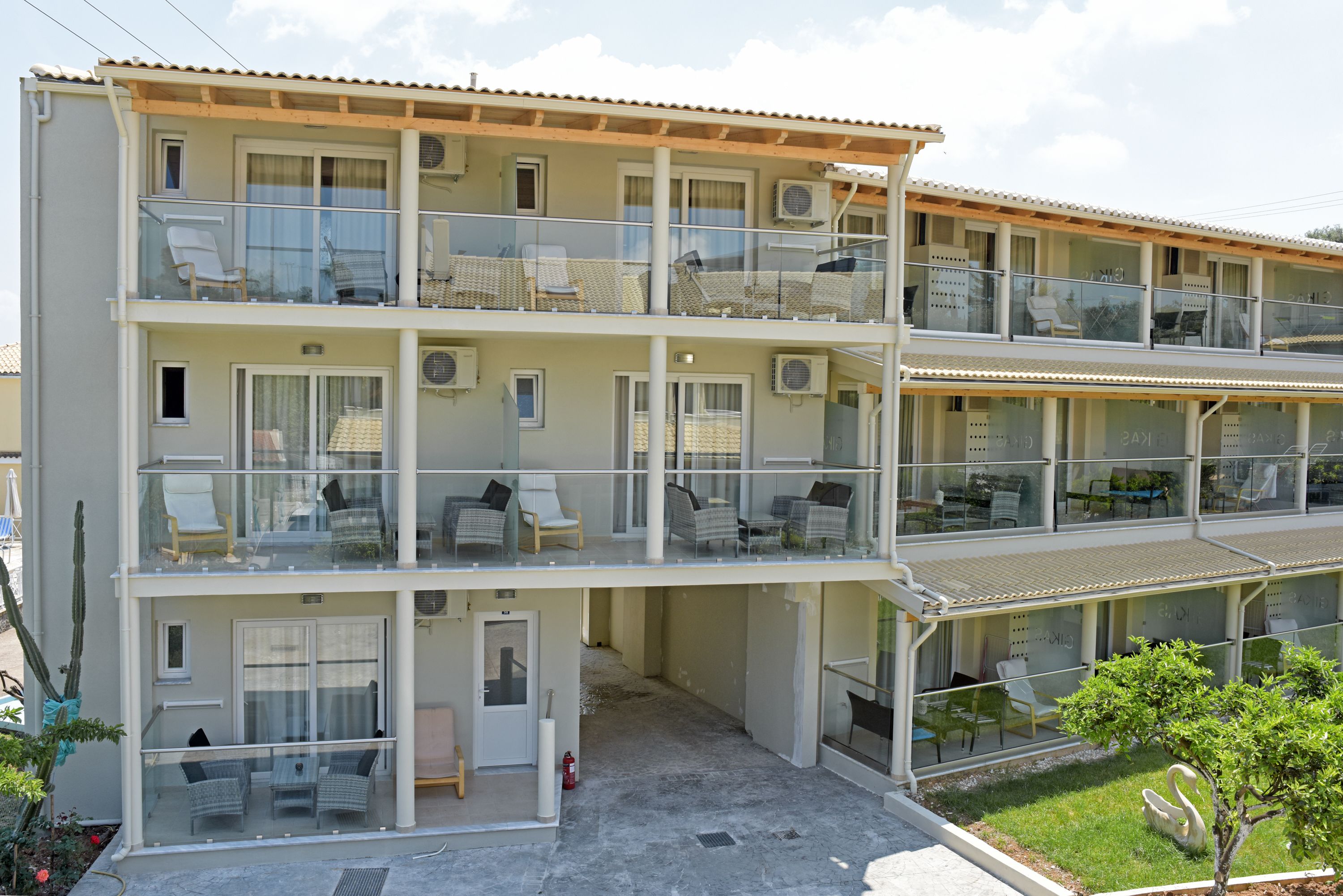Un hotel de varios pisos con balcones, mobiliario exterior y un pequeño jardín.