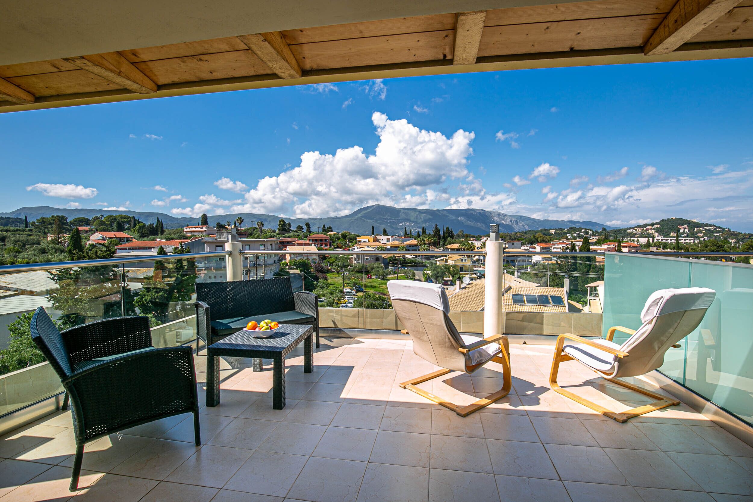 Un balcón con una mesa, dos sillas y vistas a un pueblo y montañas.