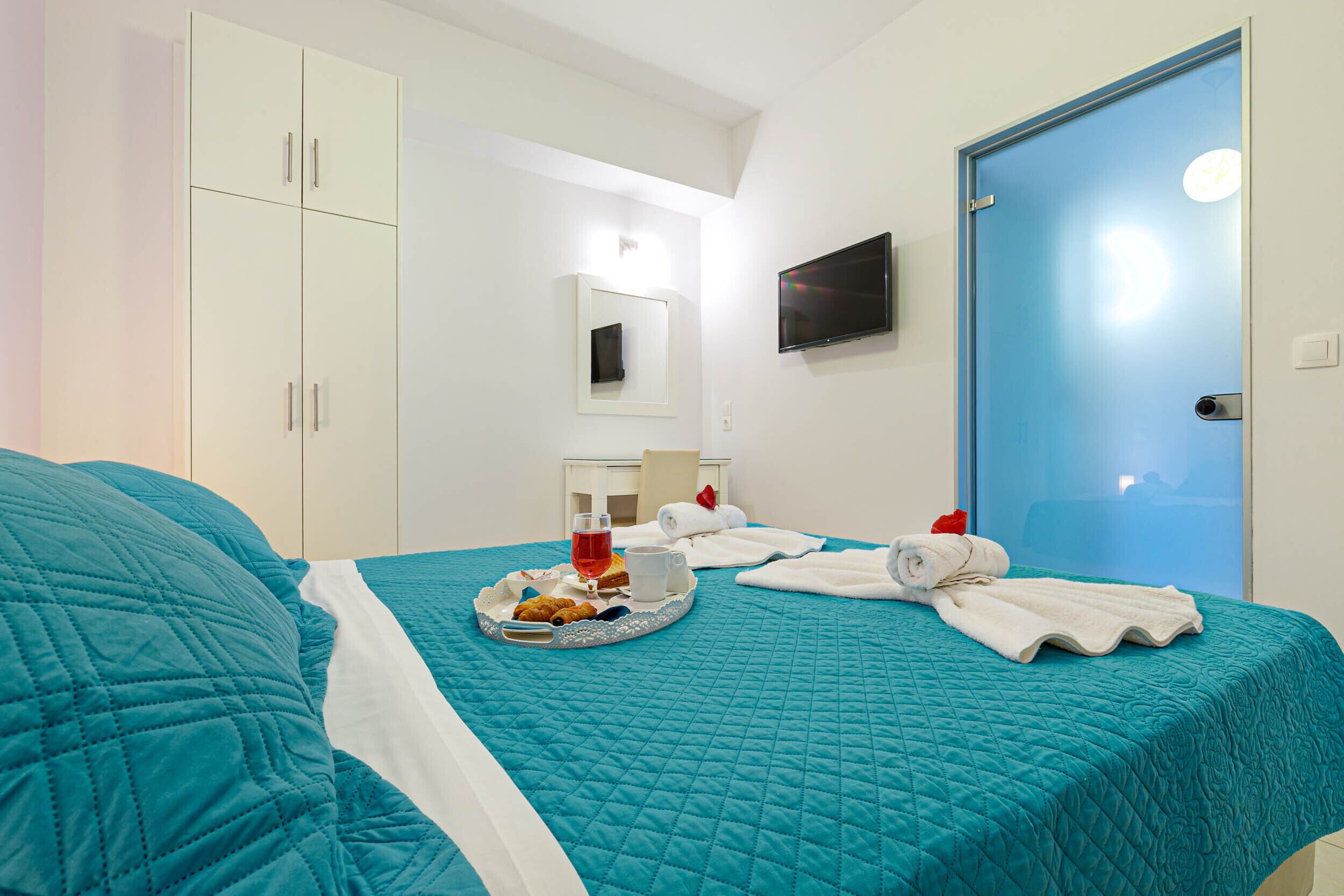 Ein Hotelzimmer mit einem Bett, einer blauen Tür, einem Fernseher und einem Tablett mit Frühstücksartikeln.