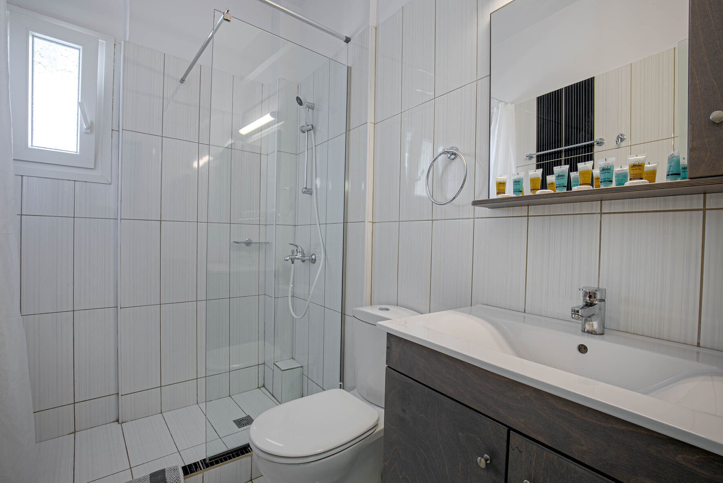 Une salle de bain moderne avec une douche à parois de verre, des toilettes blanches, un meuble-lavabo avec un miroir et une étagère contenant des articles de toilette.