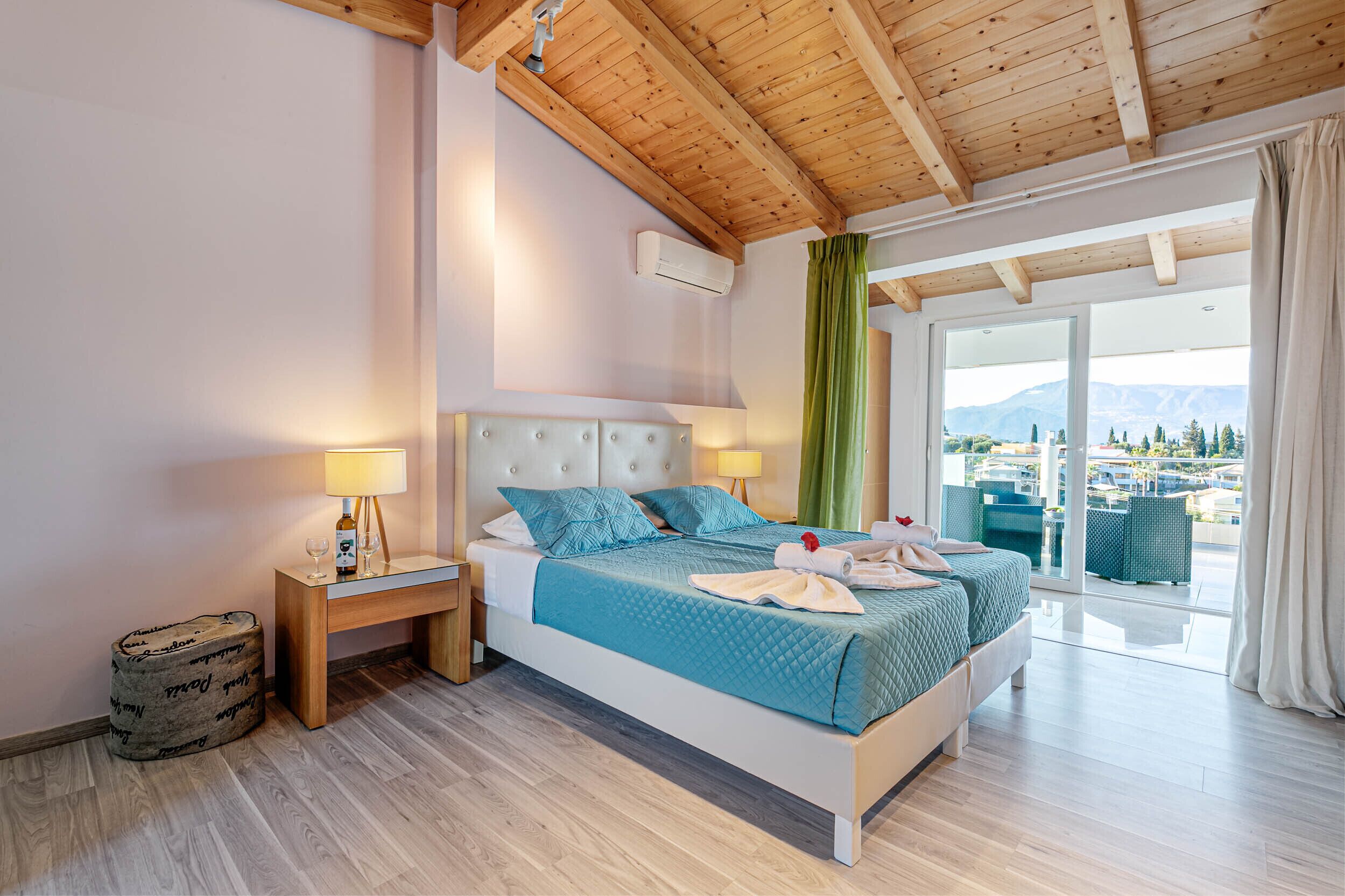 Een slaapkamer met een bed, nachtkastjes, uitzicht op de omgeving en een houten plafond.