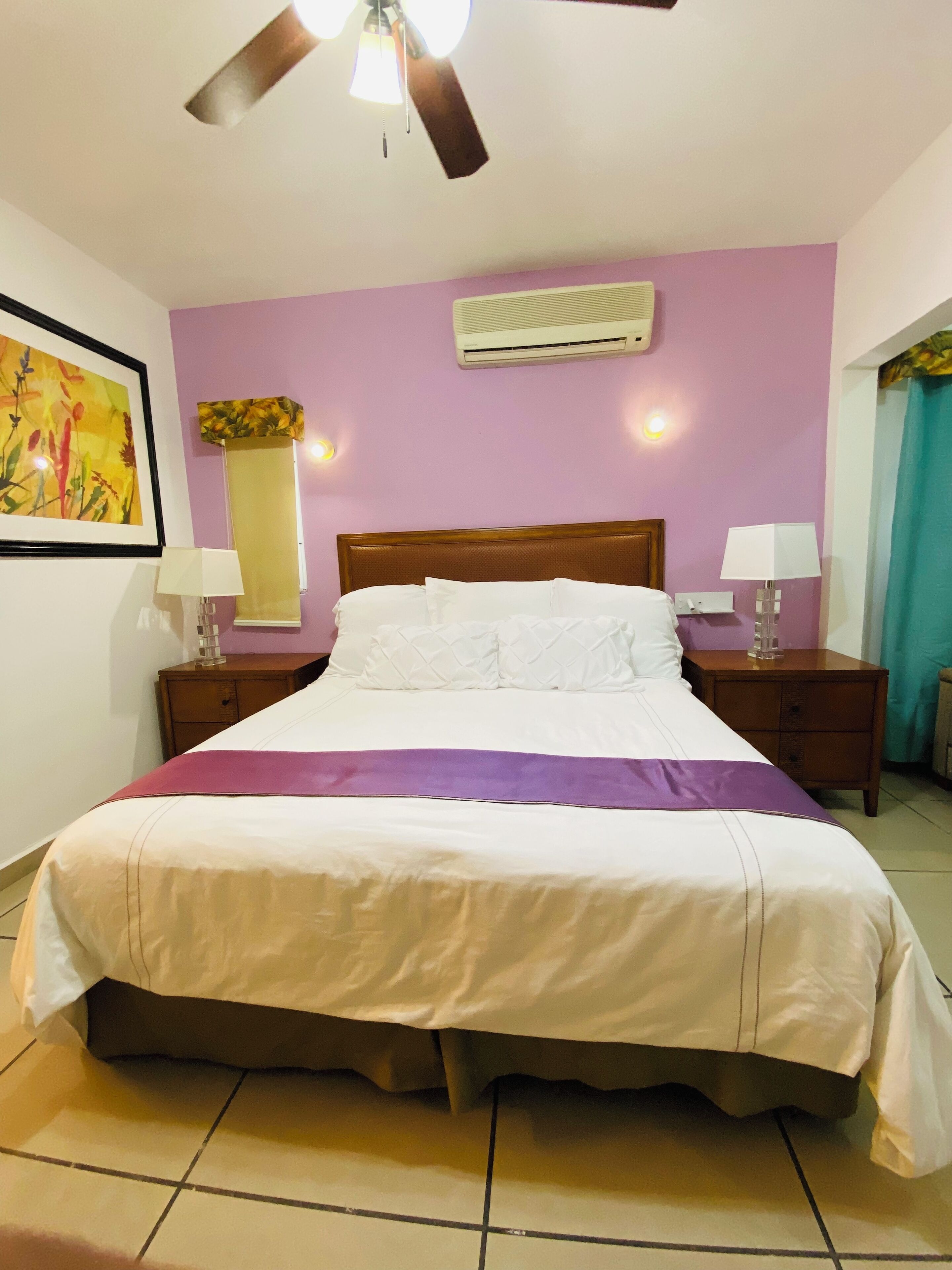 Ein Hotelzimmer mit einem Bett, zwei Nachttischen, einem Deckenventilator, einer Klimaanlage und einer Wandleuchte.
