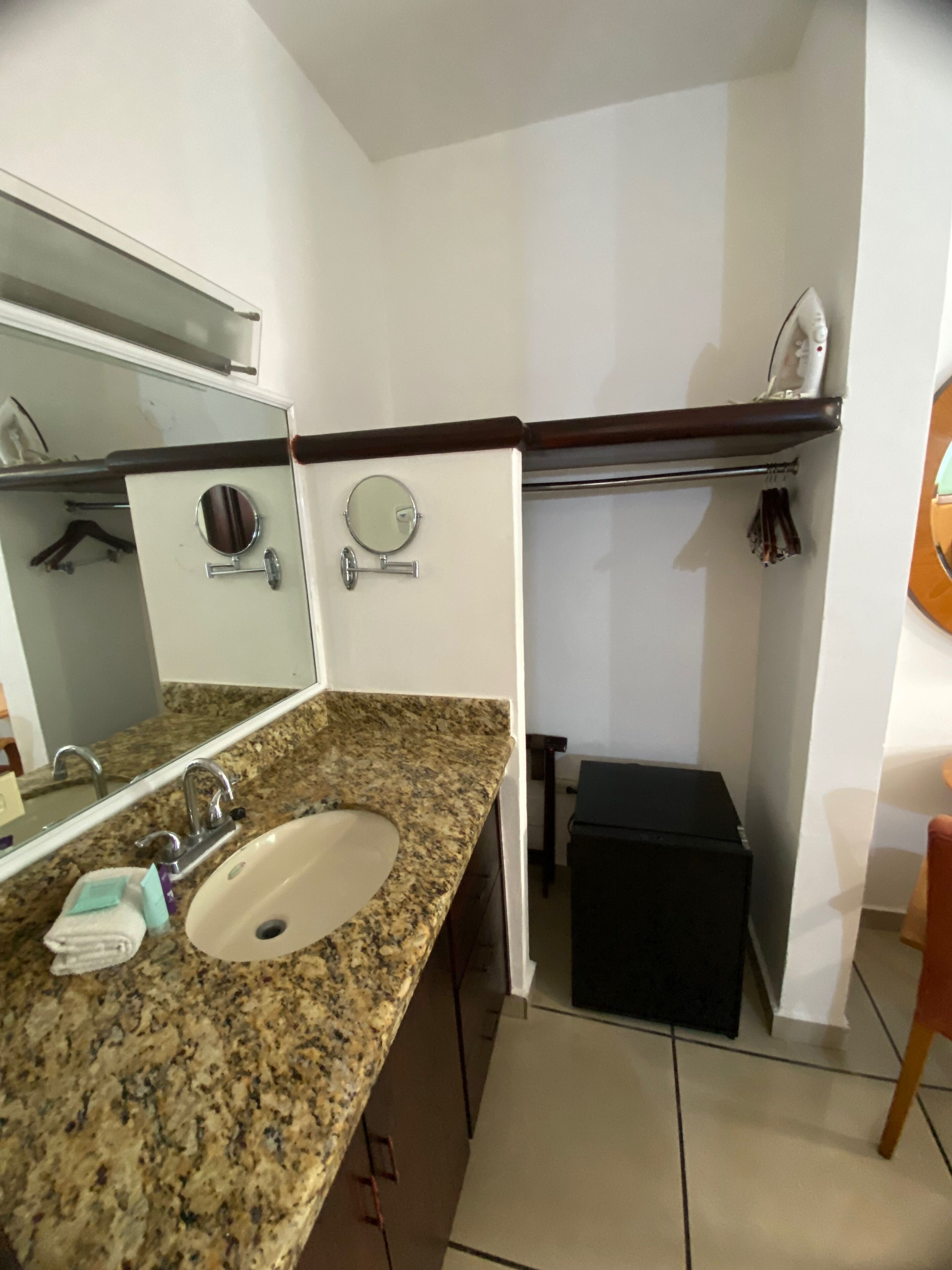 Une salle de bain avec un lavabo doté d’un plan de travail en granit, un miroir, une serviette et une petite poubelle noire.