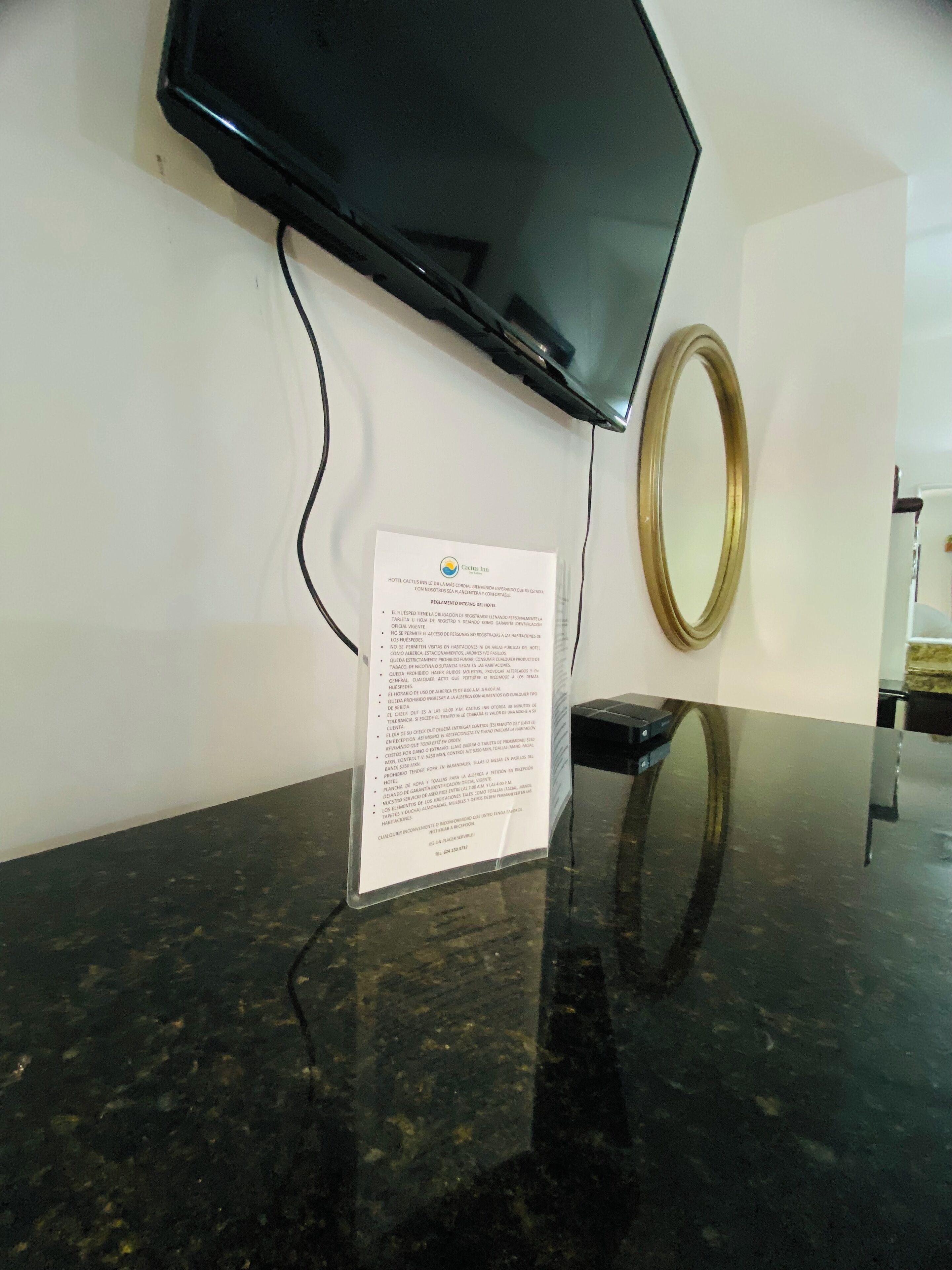 Un mostrador de recepción de mármol negro con un televisor de pantalla plana montado encima, un espejo enmarcados en la pared y un letrero con texto.